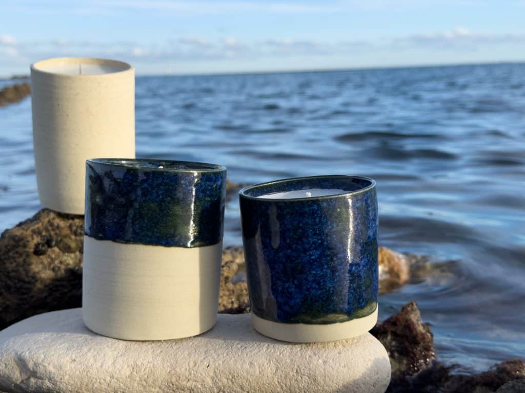 Bougies artisanales Maison Nimbe en contenants céramiques bleu profond posées face à l’océan sur l’île de Ré